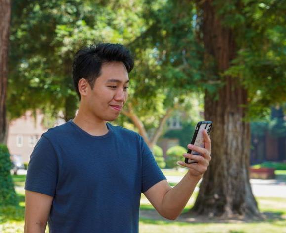 Image of male 学生 looking down at phone and smiling.